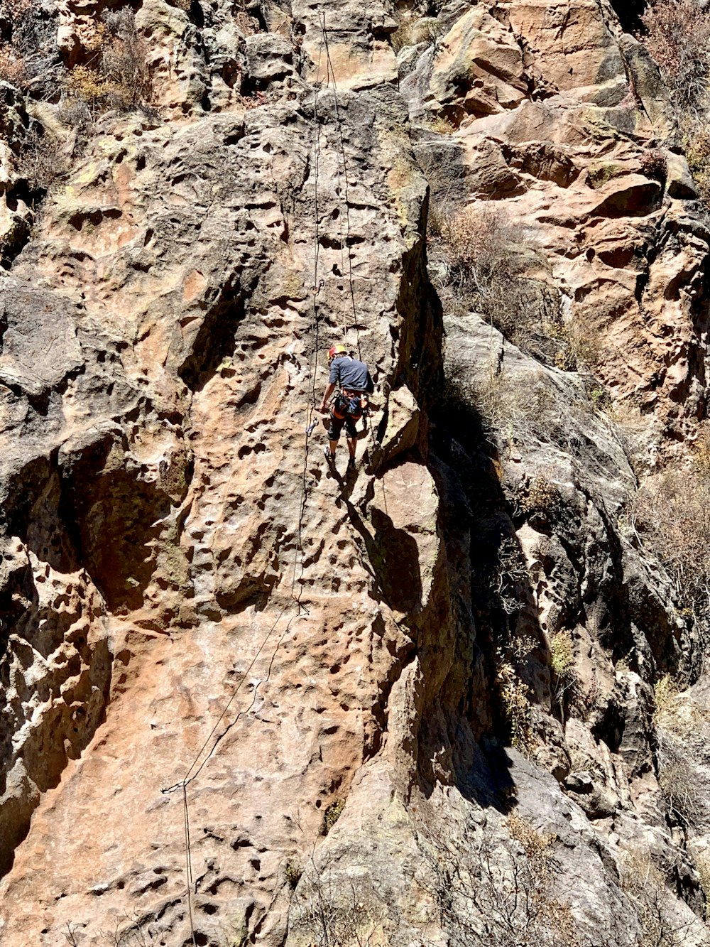 man in blue jacket climbing on brown rocky mountain during daytime