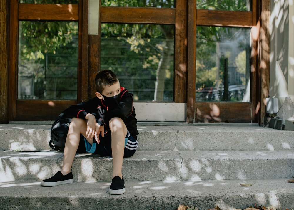 boy in black t-shirt and blue denim jeans sitting on concrete bench