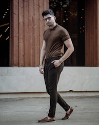 man in brown tank top and black pants standing near brown wooden door