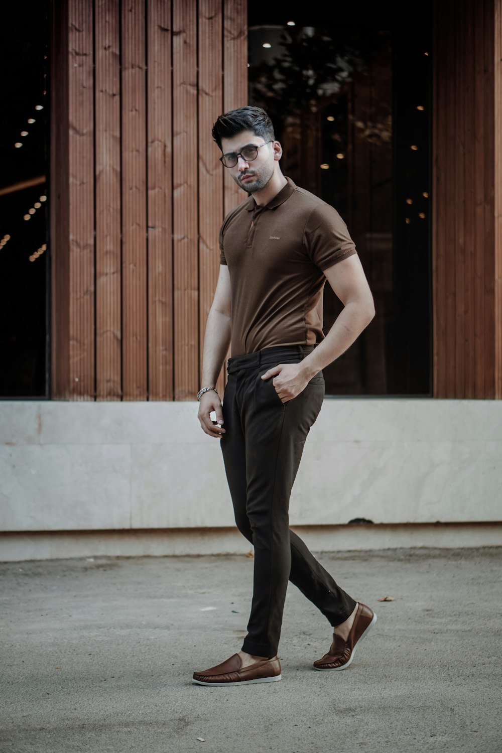 Hombre con camiseta sin mangas marrón y pantalones negros de pie cerca de la puerta de madera marrón