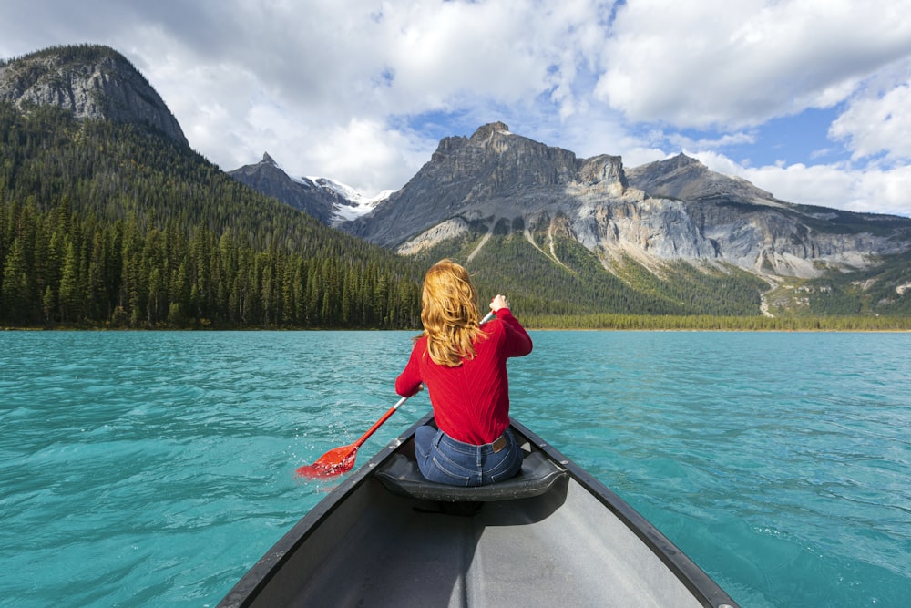 昼間、湖でボートに乗る赤い長袖シャツの女性