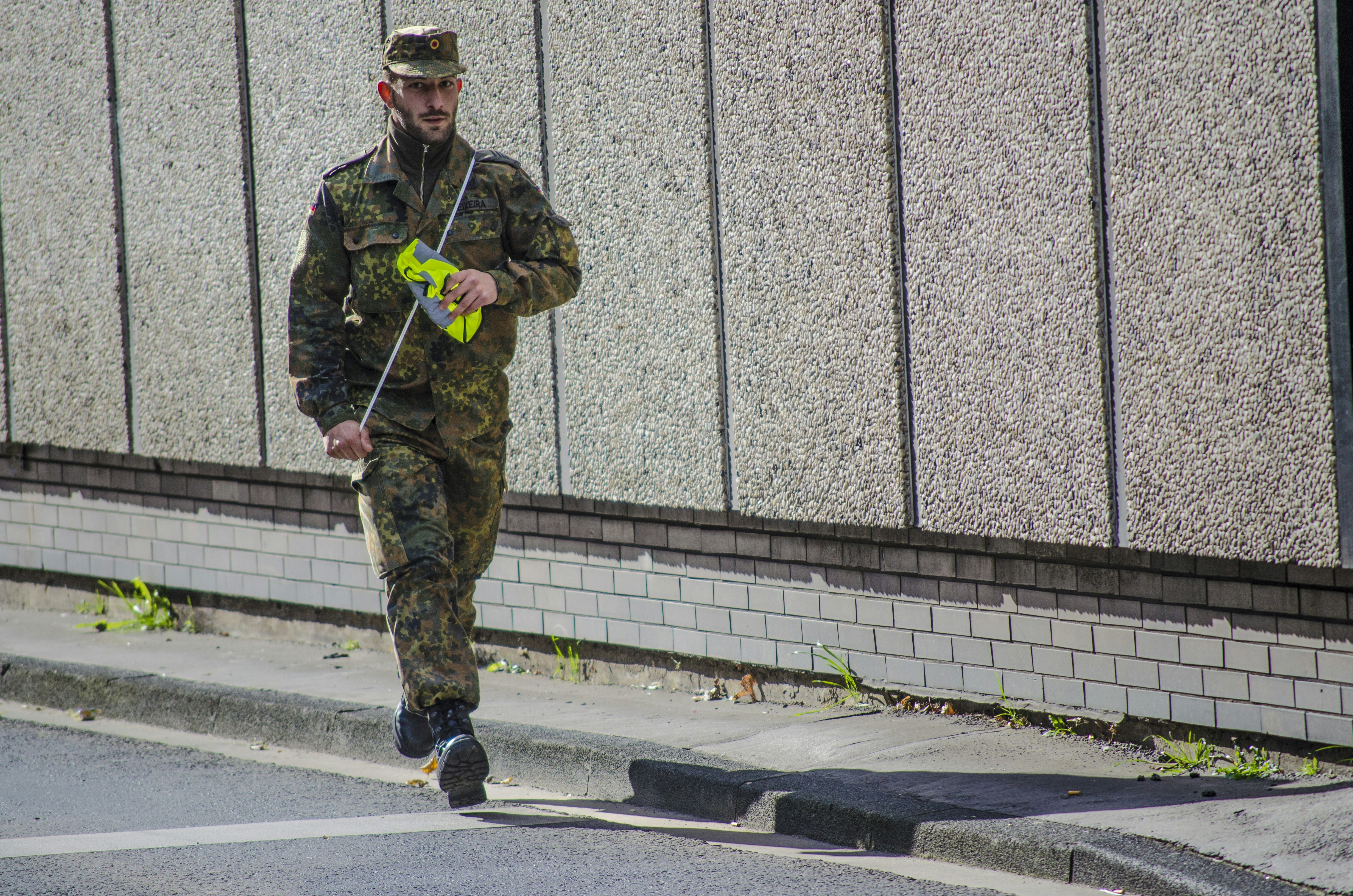 man in green and brown camouflage uniform standing on gray asphalt road during daytime