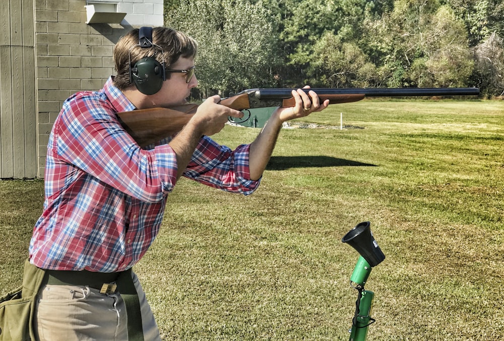 man in red blue and white plaid shirt and gray pants holding black and brown rifle