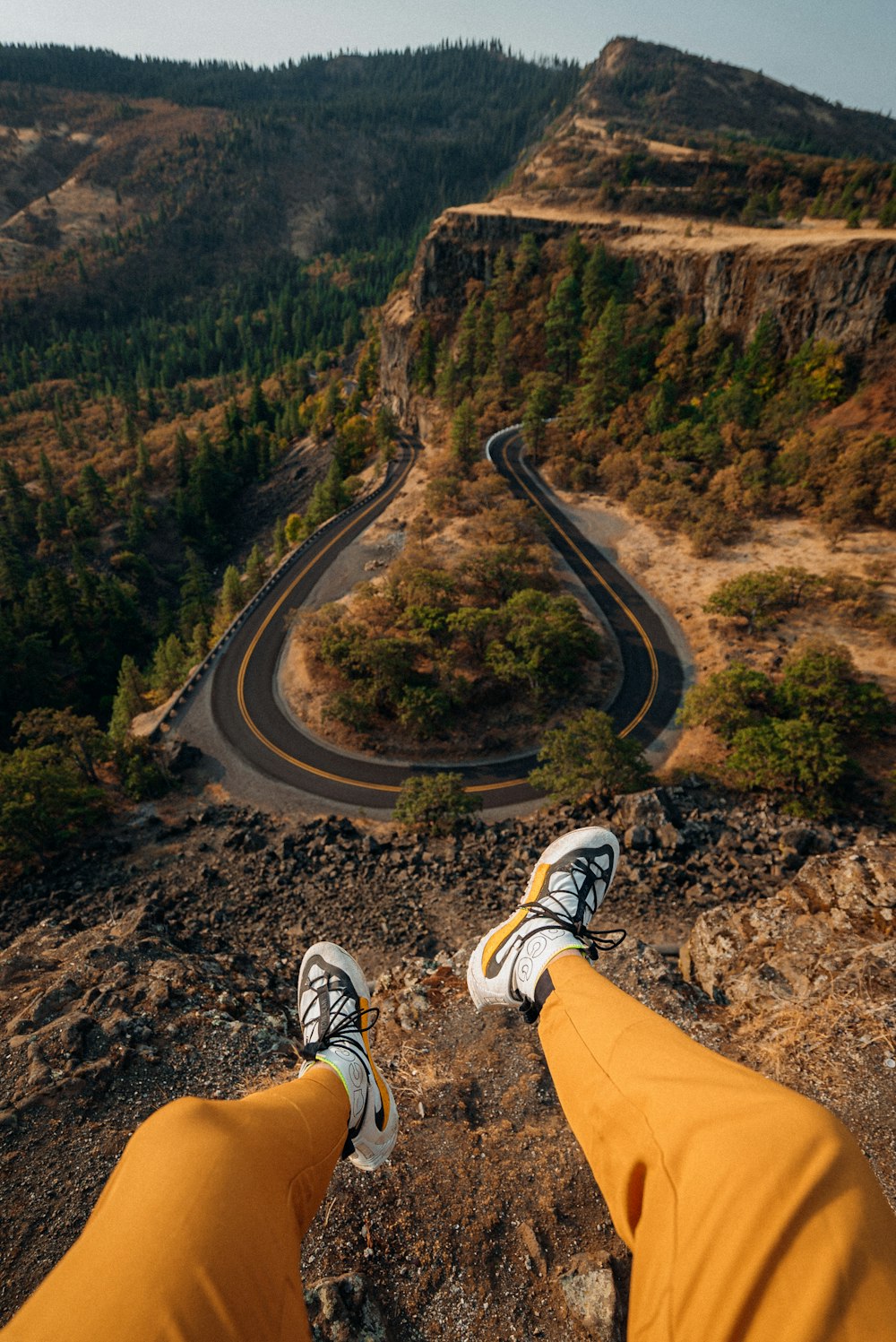 person in orange pants and white and black sneakers sitting on brown rock mountain during daytime