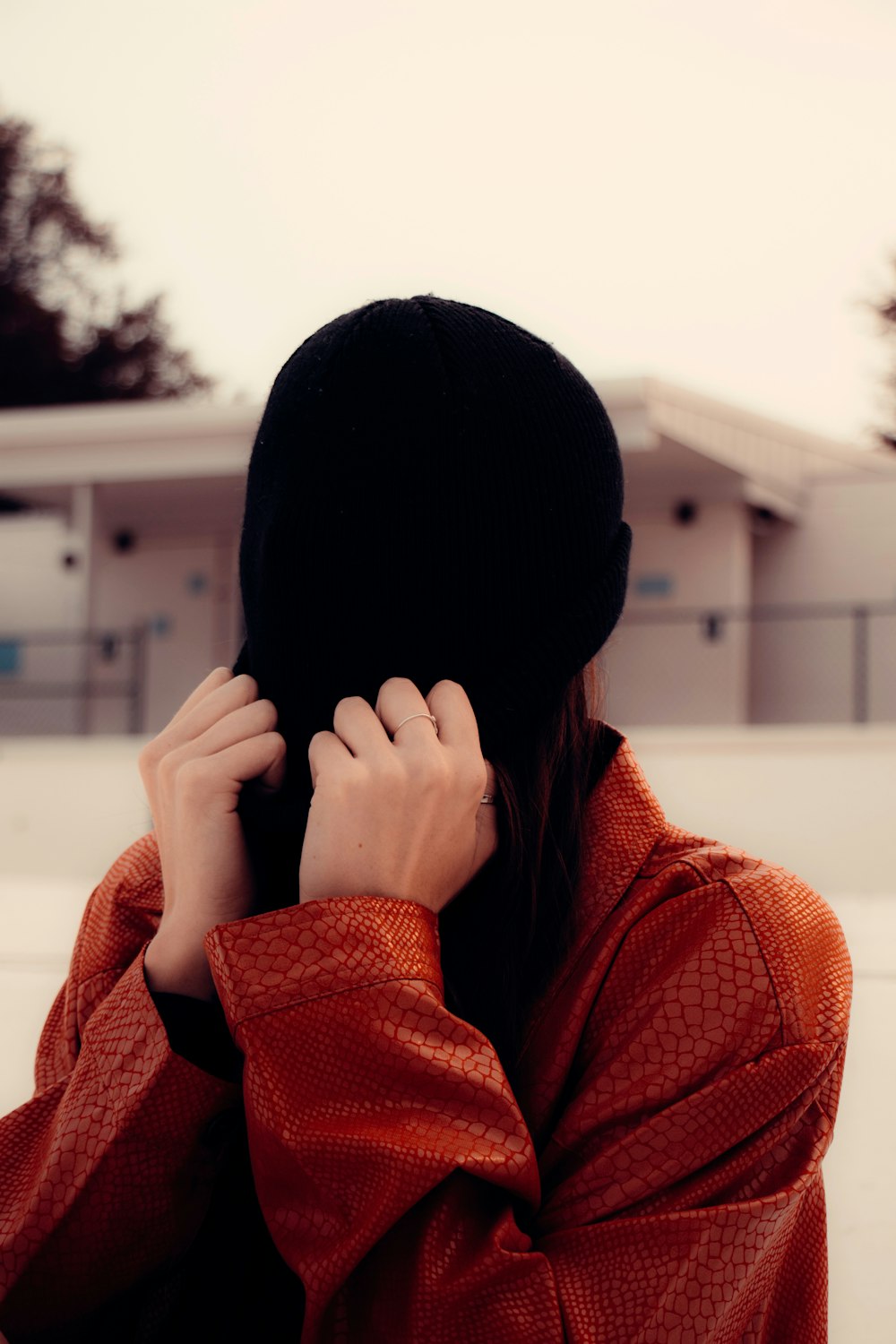 woman in red knit sweater covering face with black knit cap
