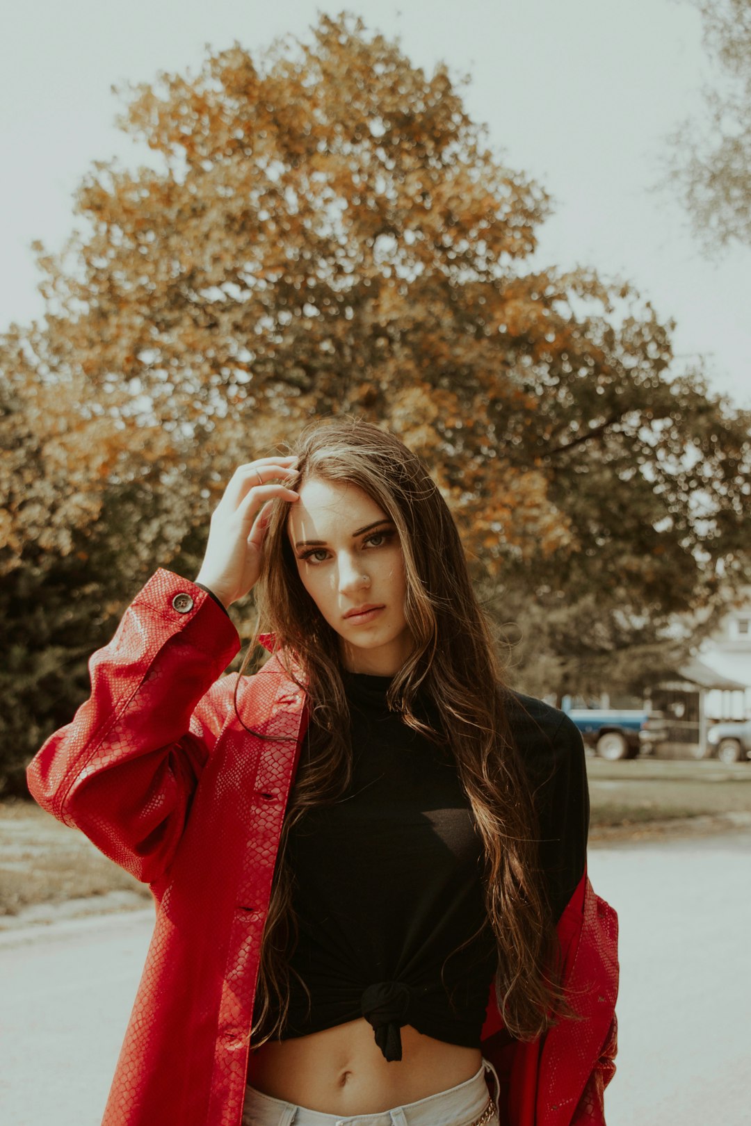 woman in red leather jacket standing near brown trees during daytime
