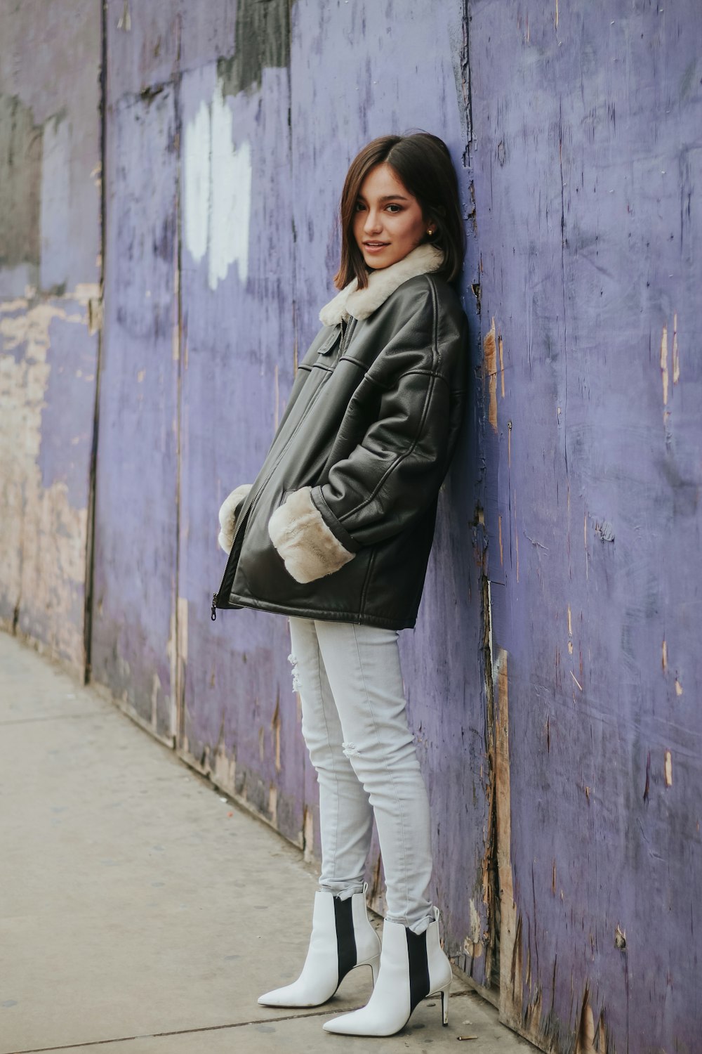 woman in gray jacket and white pants standing beside blue wooden door