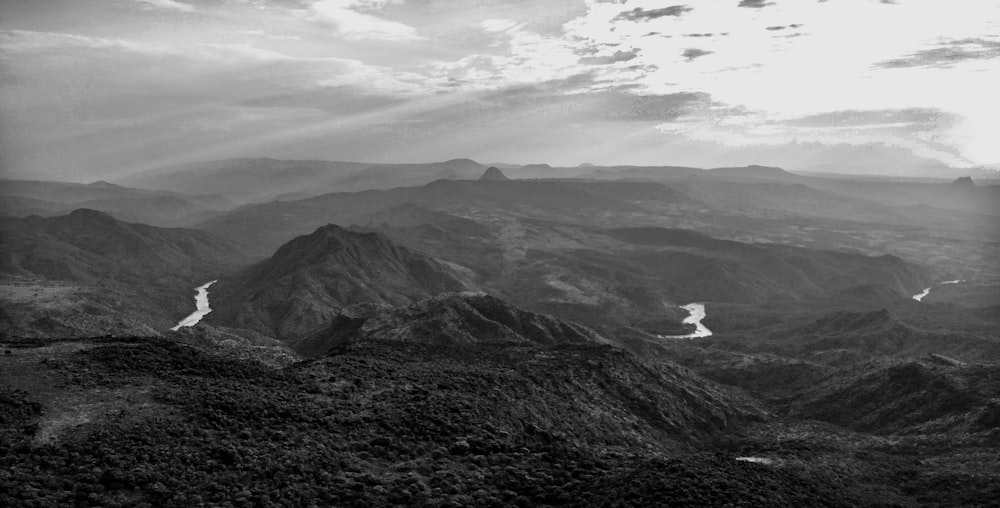 grayscale photo of person surfing on sea near mountain