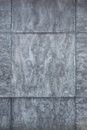 Gray textured tiles with a stone-like appearance, arranged in a grid pattern, displaying subtle variations in shading and surface texture.