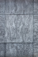 Gray textured tiles with a stone-like appearance, arranged in a grid pattern, displaying subtle variations in shading and surface texture.