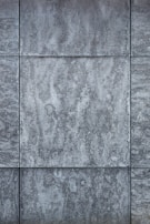 Gray textured tiles with a stone-like appearance, arranged in a grid pattern, displaying subtle variations in shading and surface texture.