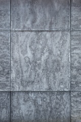 Gray textured tiles with a stone-like appearance, arranged in a grid pattern, displaying subtle variations in shading and surface texture.