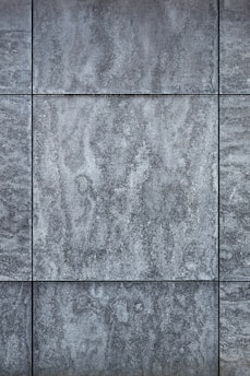 Gray textured tiles with a stone-like appearance, arranged in a grid pattern, displaying subtle variations in shading and surface texture.