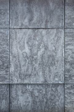 Gray textured tiles with a stone-like appearance, arranged in a grid pattern, displaying subtle variations in shading and surface texture.