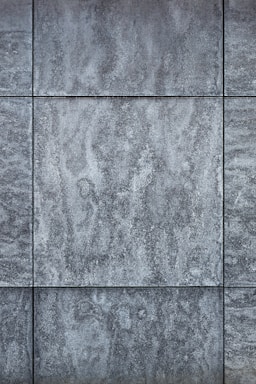 Gray textured tiles with a stone-like appearance, arranged in a grid pattern, displaying subtle variations in shading and surface texture.
