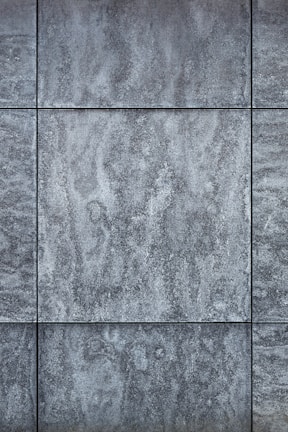 Gray textured tiles with a stone-like appearance, arranged in a grid pattern, displaying subtle variations in shading and surface texture.