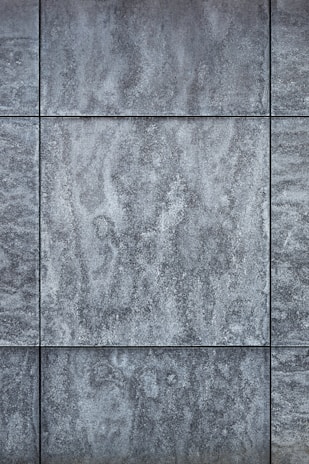Gray textured tiles with a stone-like appearance, arranged in a grid pattern, displaying subtle variations in shading and surface texture.
