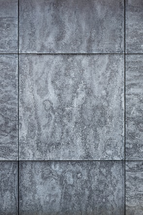 Gray textured tiles with a stone-like appearance, arranged in a grid pattern, displaying subtle variations in shading and surface texture.