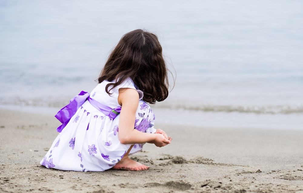 昼間のビーチショアに座っている紫色のドレスを着た女の子