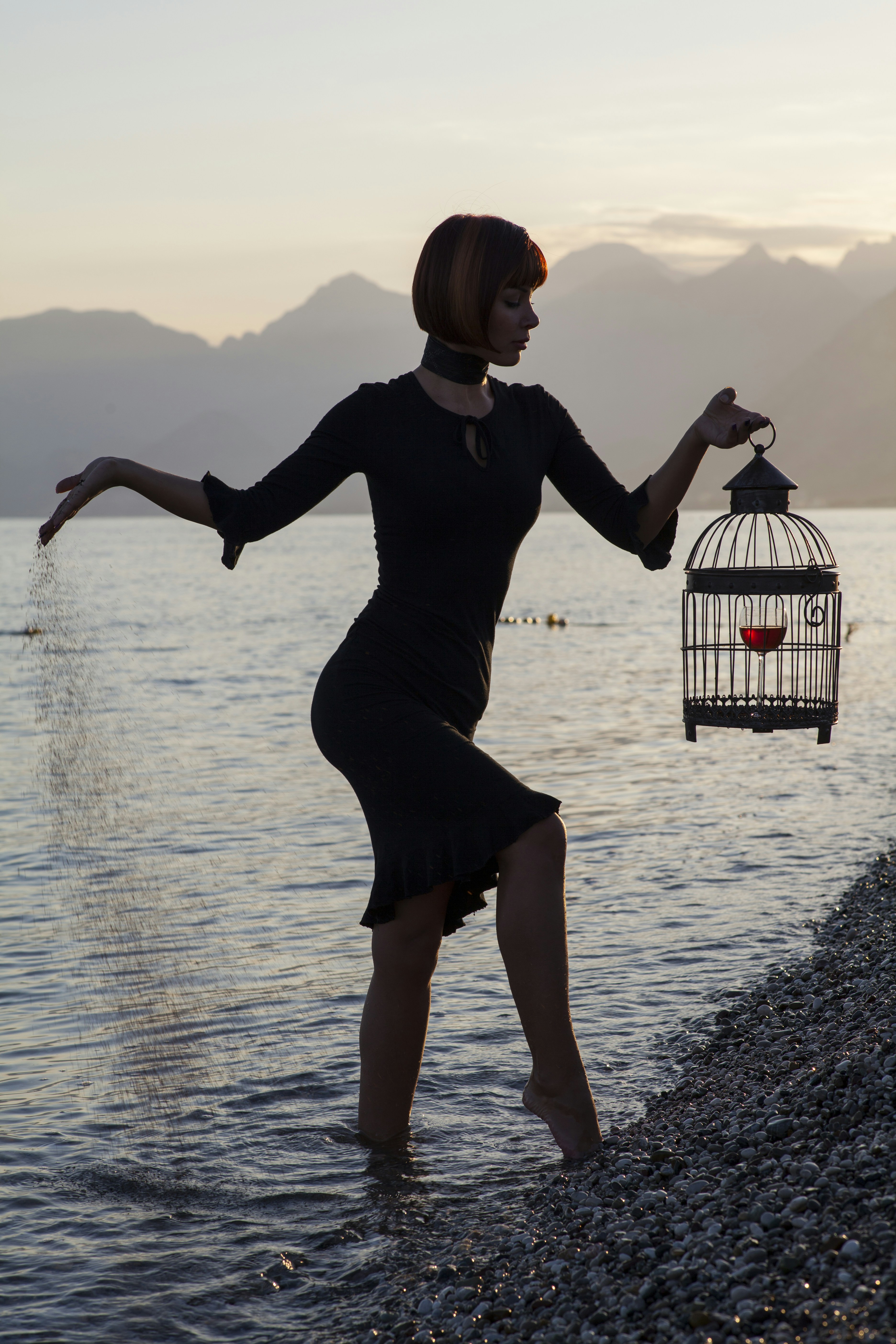 great photo recipe,how to photograph a conceptual portrait; woman in black long sleeve dress holding white and black bird cage on water during daytime