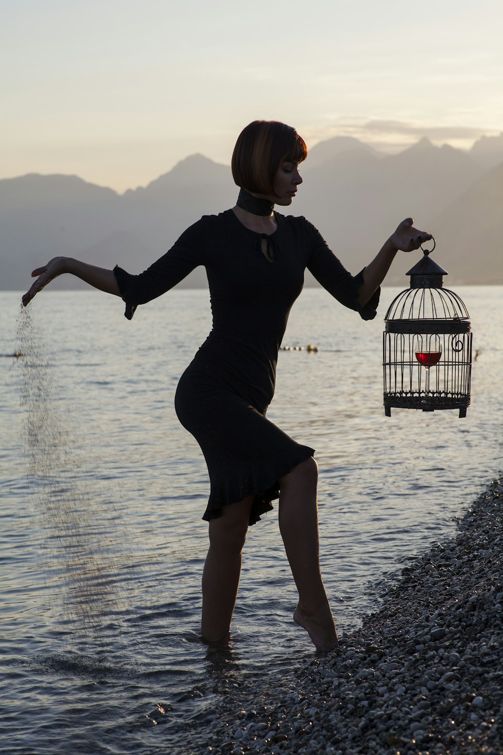 woman in black long sleeve dress holding white and black bird cage on water during daytime