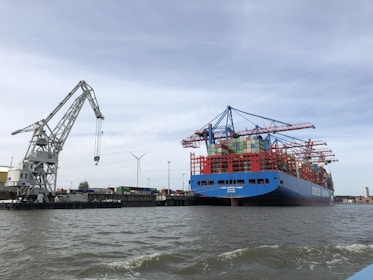 blue and red cargo ship on sea under blue sky during daytime
