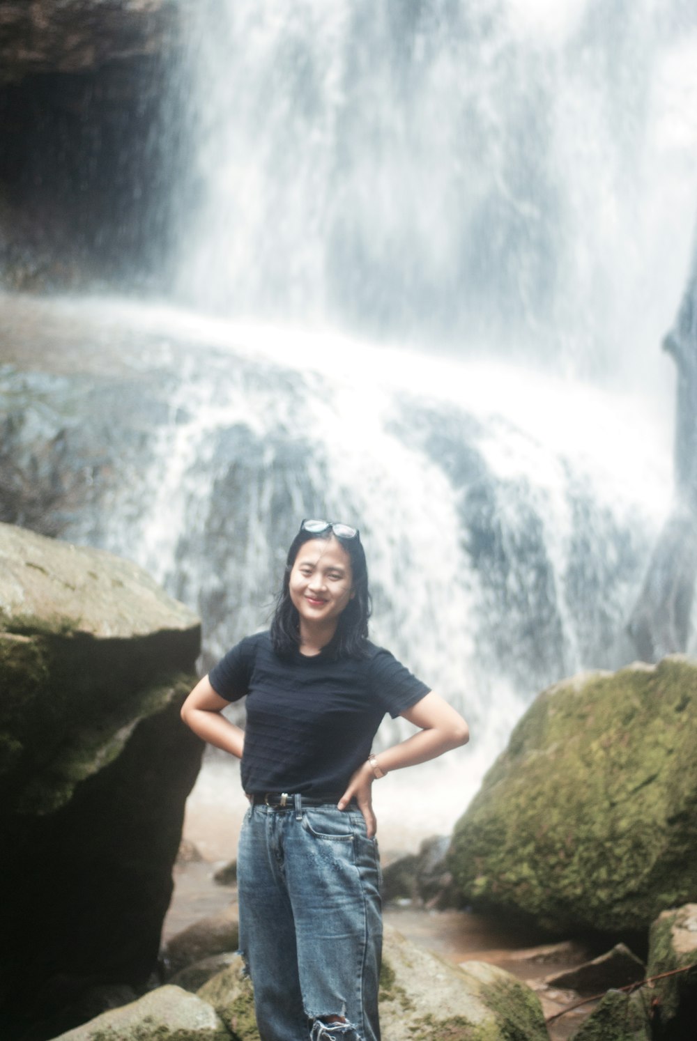 Donna in maglietta girocollo nera in piedi sulla roccia vicino alle cascate durante il giorno
