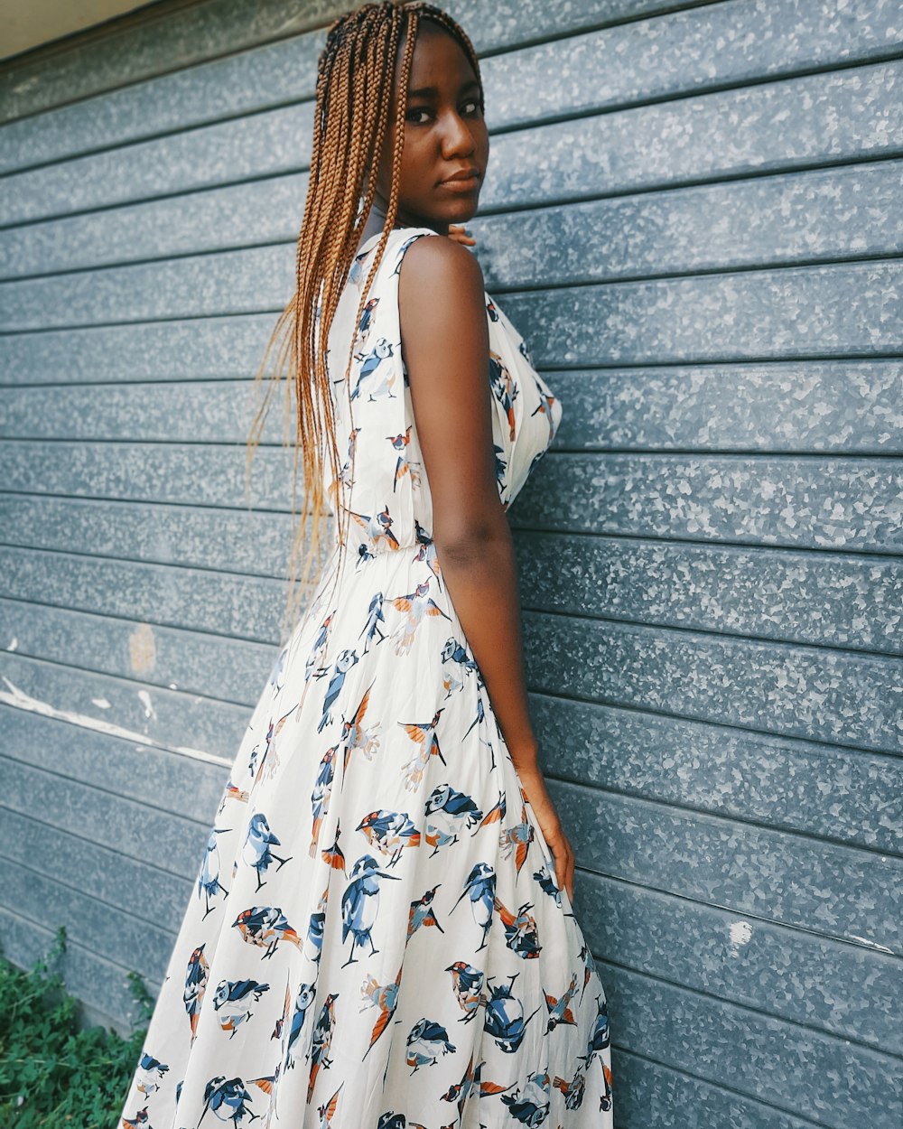 woman in white and yellow floral sleeveless dress standing beside gray wall