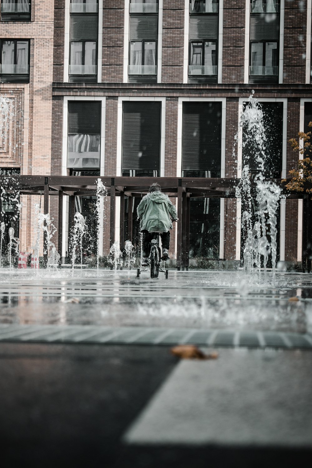 Persona in giacca verde che cammina sulla strada bagnata durante il giorno