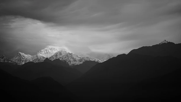 A dramatic black and white landscape shot showcasing rugged mountains under a moody sky.