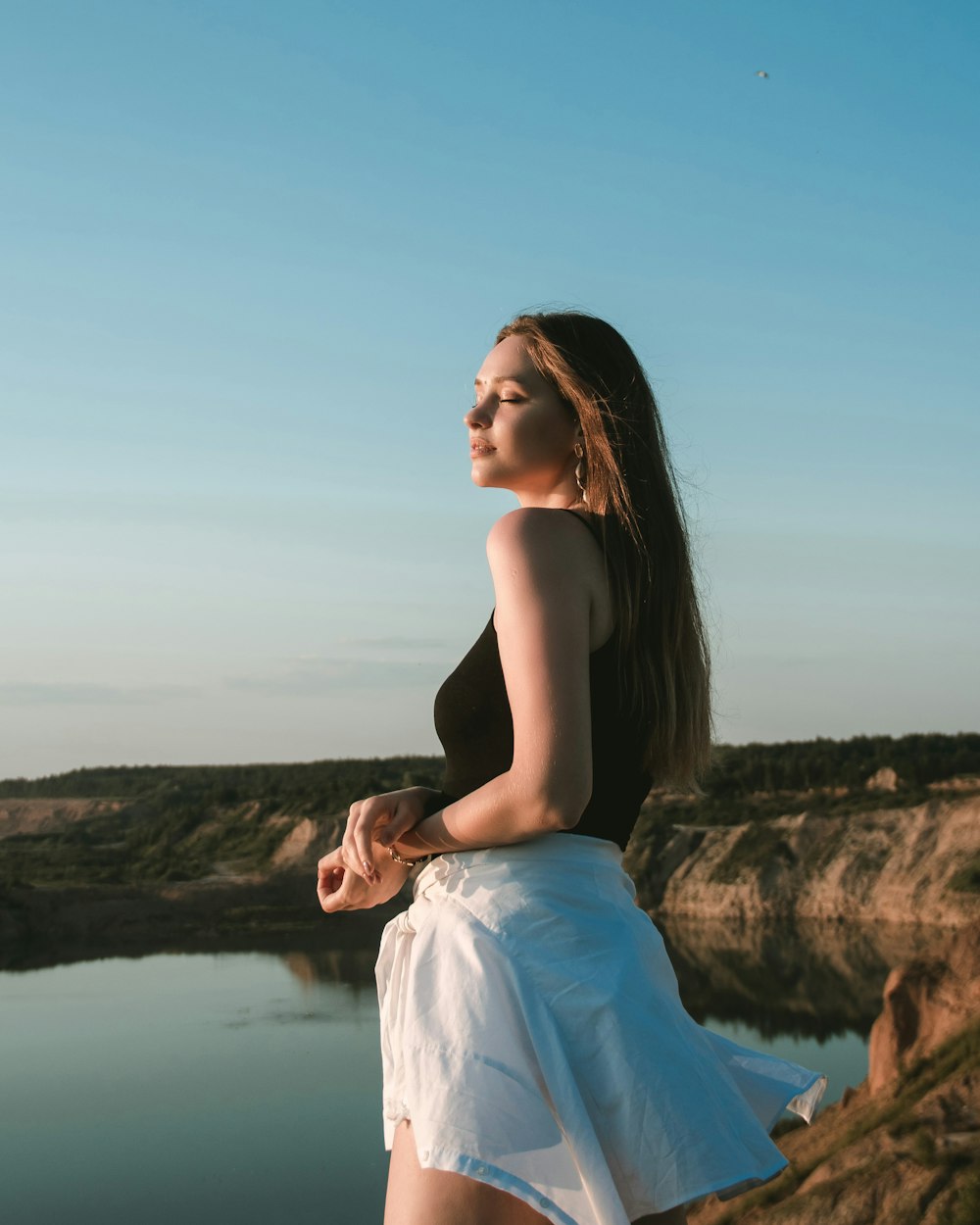 woman in white dress standing on rock near body of water during daytime