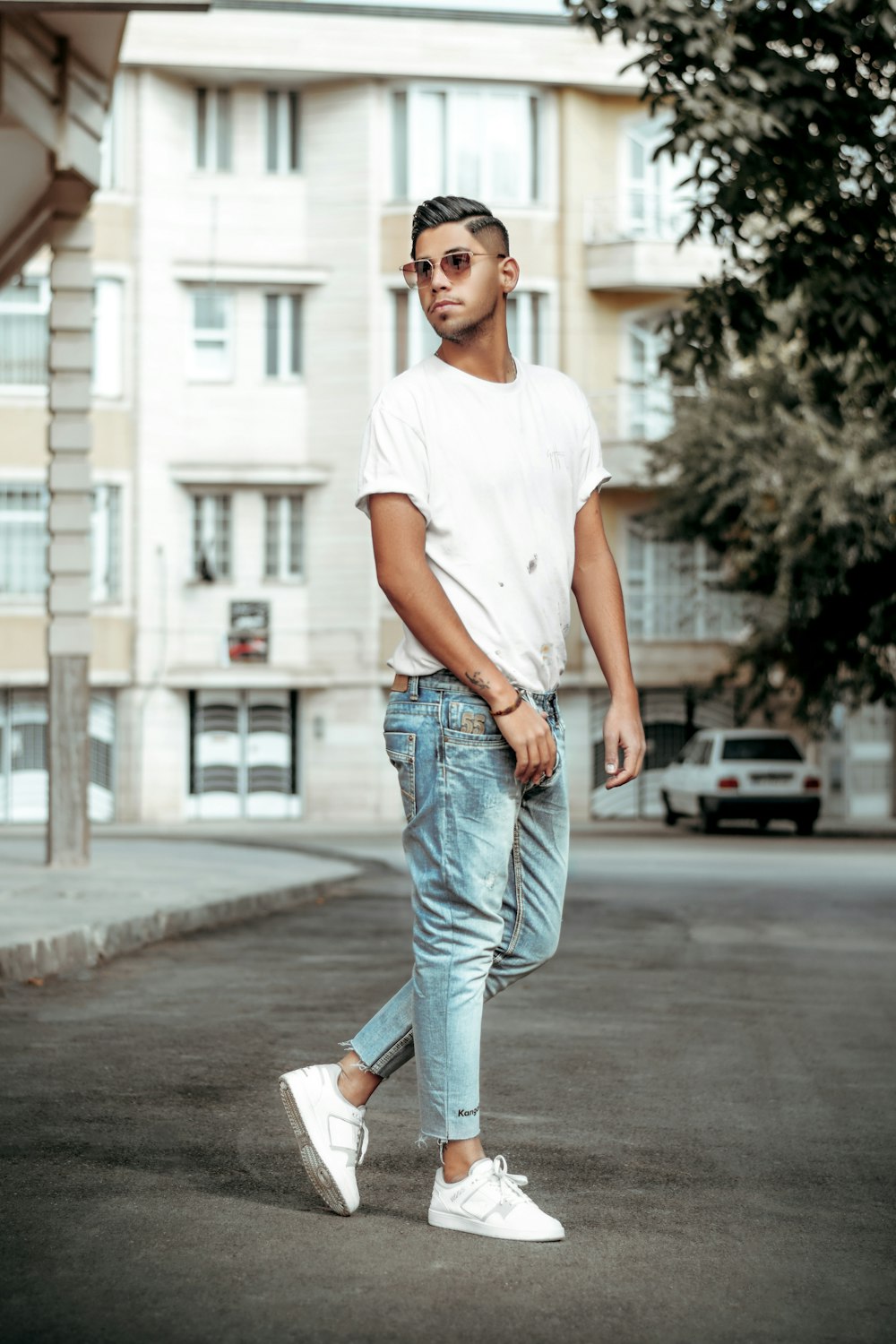 woman in white crew neck t-shirt and blue denim jeans standing on sidewalk during daytime