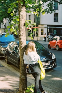 woman in white long sleeve shirt and green pants standing beside black car during daytime