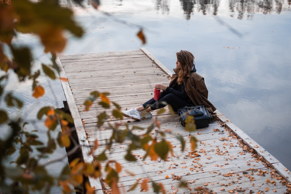 woman in black jacket sitting on dock during daytime