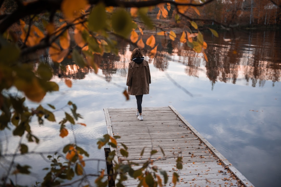 woman in brown coat walking on wooden pathway during daytime