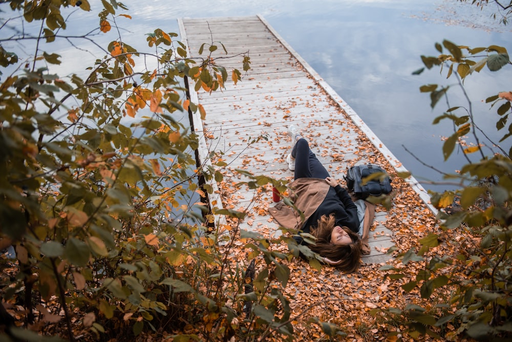 person in black jacket lying on brown wooden dock during daytime
