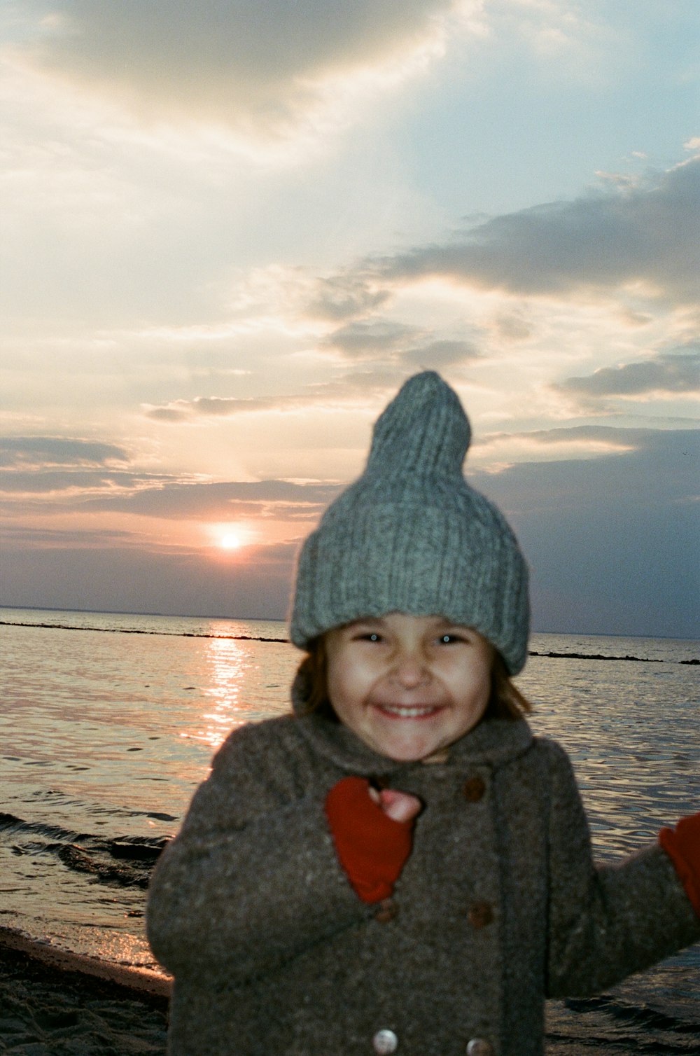 girl in gray knit cap and gray jacket standing on beach during daytime