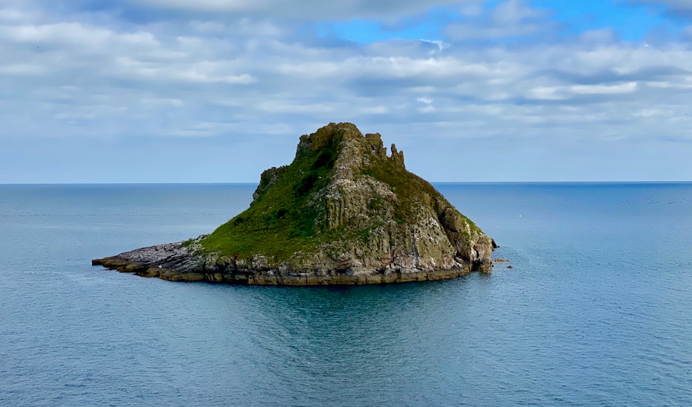 green and brown rock formation on blue sea under white clouds and blue sky during daytime