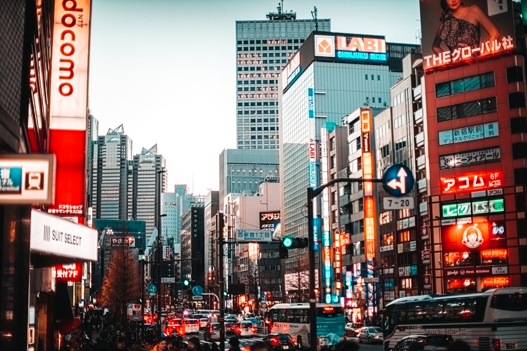 cars on road between high rise buildings during daytime, Shinjuku, Japan at 5pm winter with night lights.