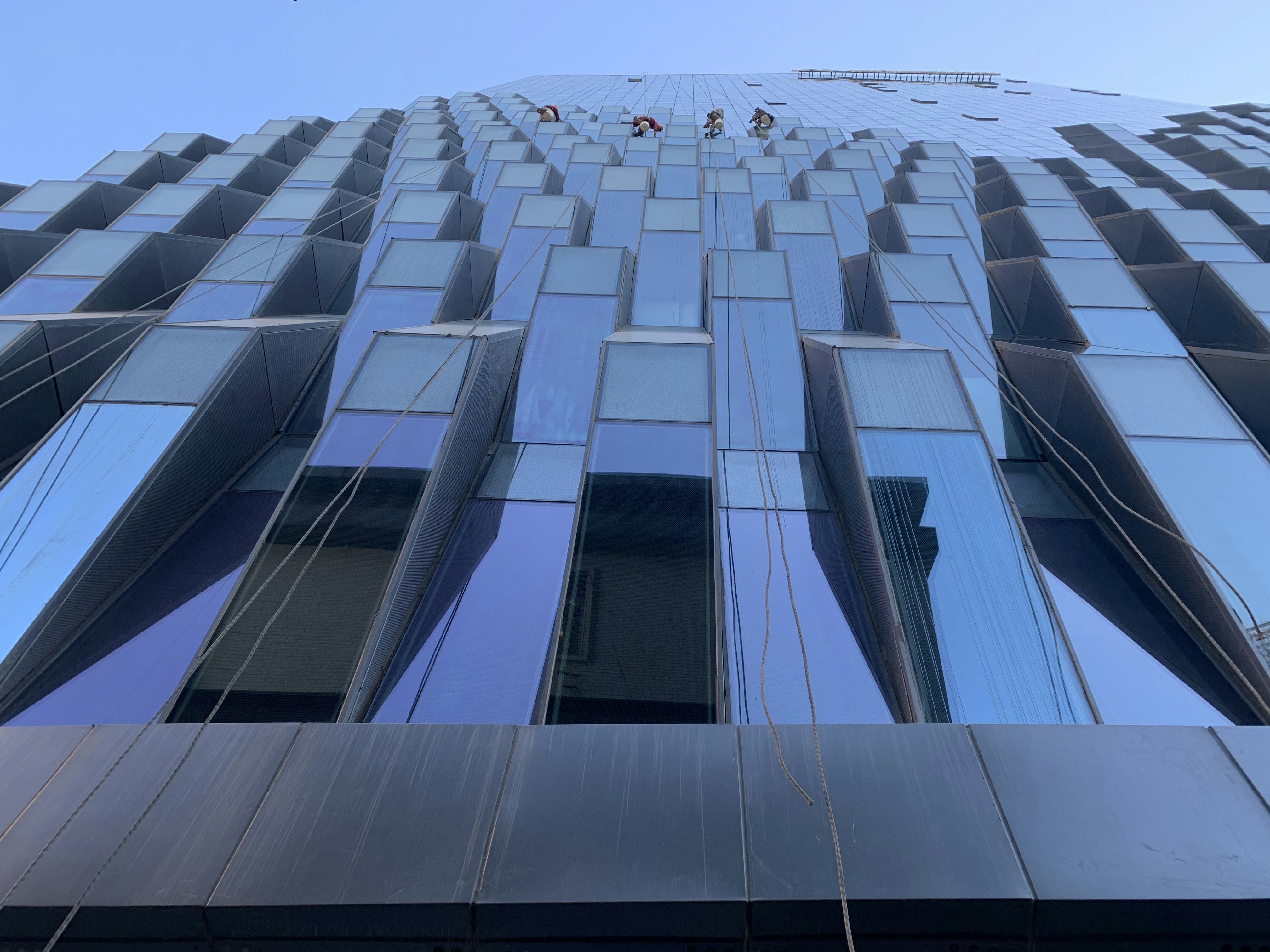 Professional window cleaner on ladder outside building, bright blue sky reflection in clean glass