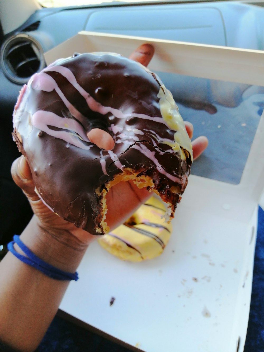 a person holding a chocolate covered doughnut in their hand