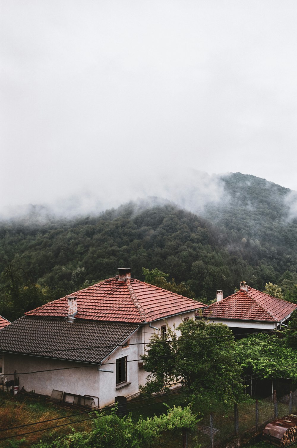 brown roof house near green mountain under white clouds during daytime