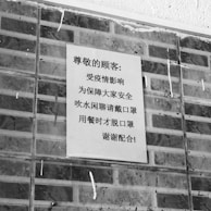 A black and white poster containing text in Chinese is affixed to a brick wall. The poster addresses safety precautions and mentions wearing masks.