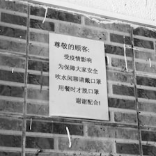 A black and white poster containing text in Chinese is affixed to a brick wall. The poster addresses safety precautions and mentions wearing masks.
