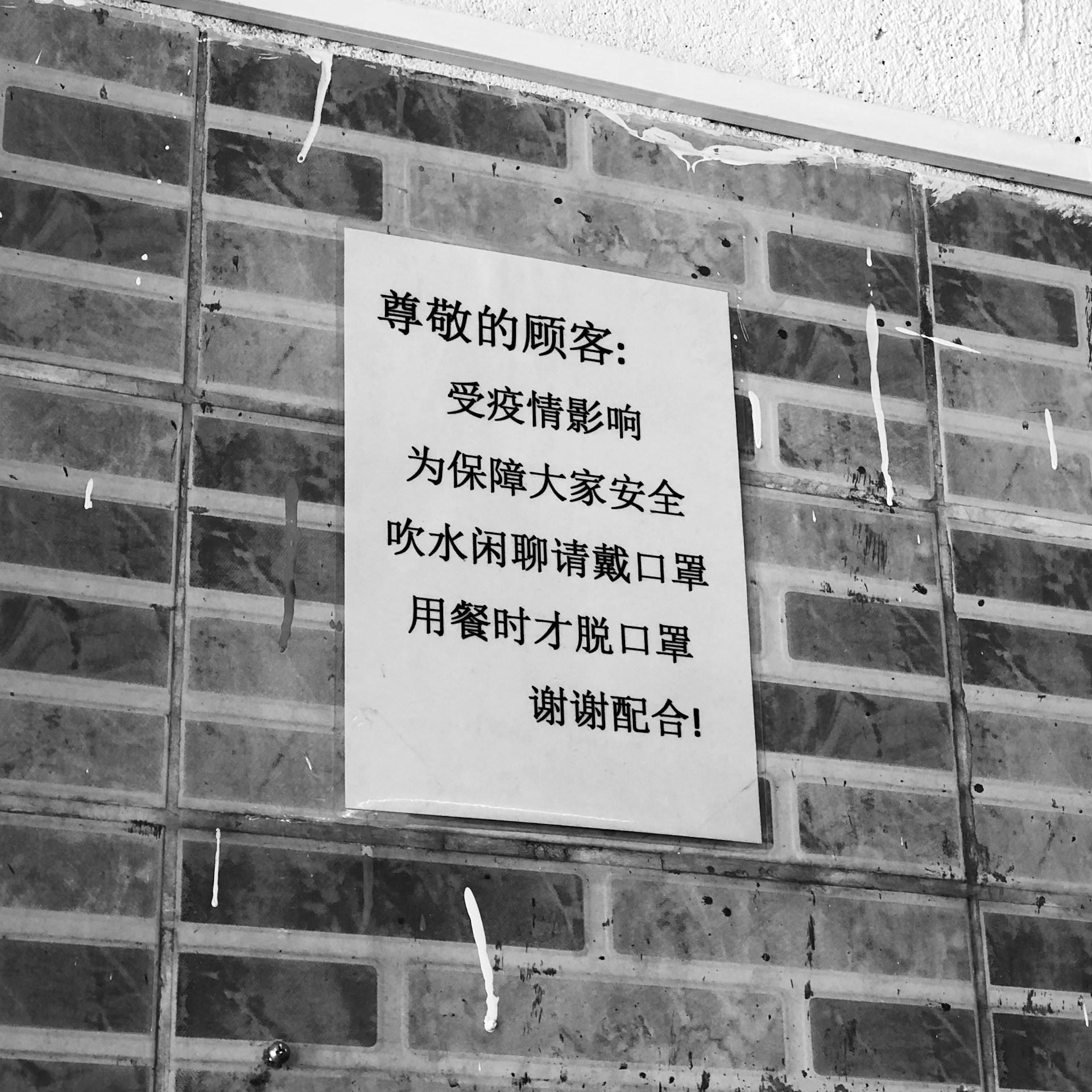 A black and white poster containing text in Chinese is affixed to a brick wall. The poster addresses safety precautions and mentions wearing masks.