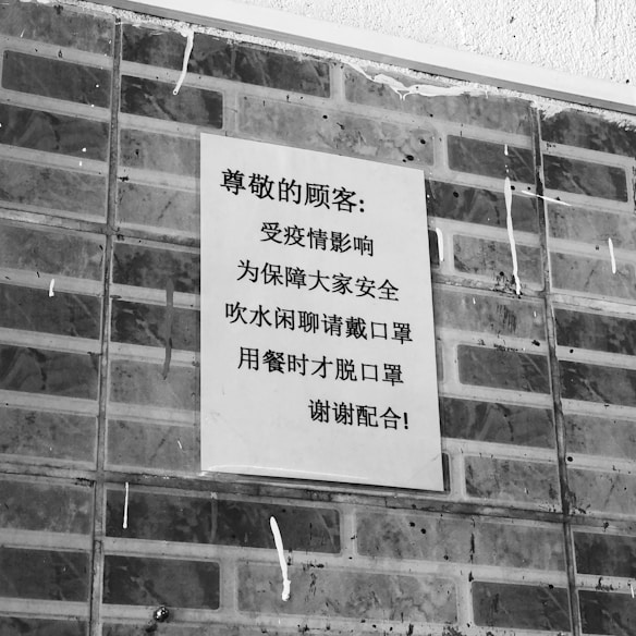 A black and white poster containing text in Chinese is affixed to a brick wall. The poster addresses safety precautions and mentions wearing masks.