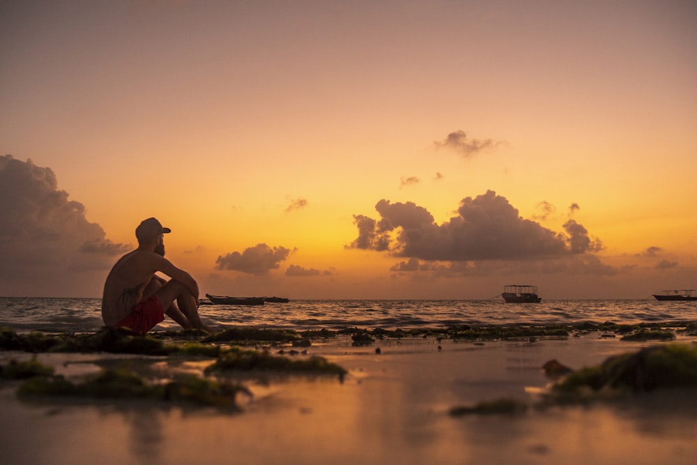 silhouette of man sitting on shore during sunset
