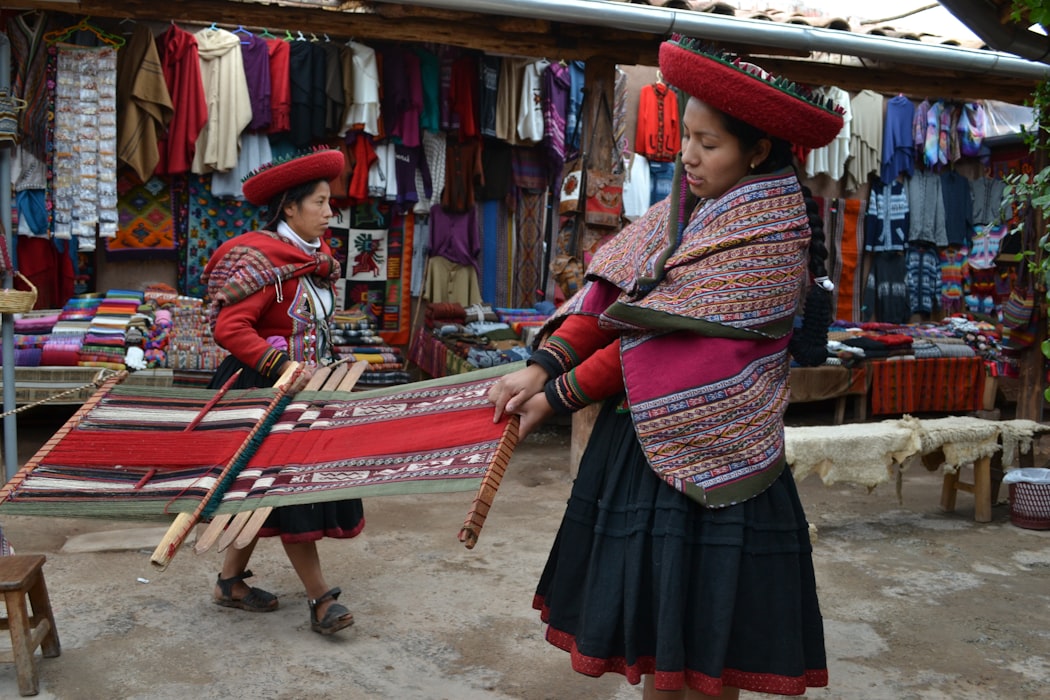 Two women wearing traditional Peruvian dress, hand weaving in the Sacred Valley of the Incas.