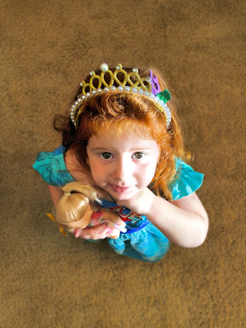 A little girl wearing a sparkling crown and a princess dress, smiling brightly.