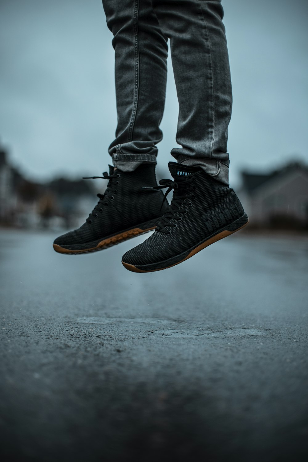 person in blue denim jeans and black leather boots standing on gray asphalt road during daytime